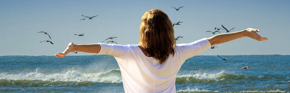 Femme face à la mer avec les bras écartés