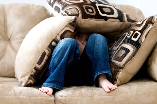 une jeune fille assise sur un canapé est recouverte de coussins
