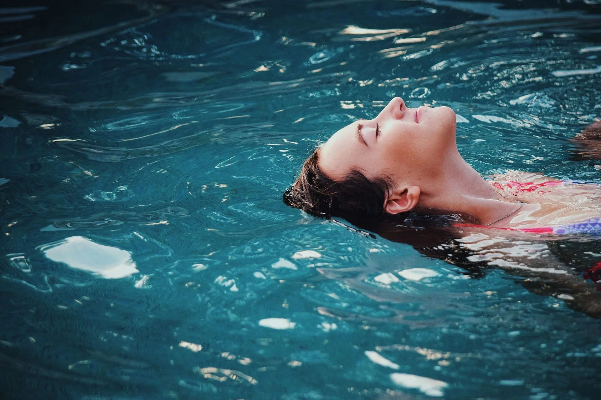 Femme les yeux fermés, allongée sur le dos dans l’eau, exprimant un état de détente profonde et de lâcher-prise